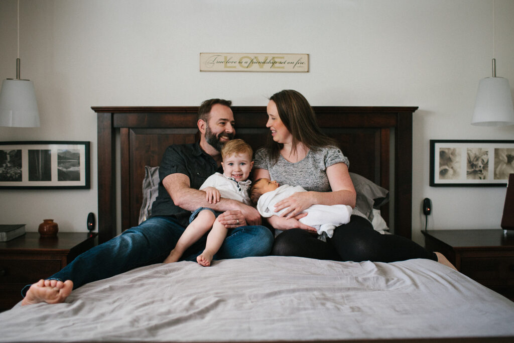 Dad holding baby daughter while the family snuggles on the bed during Lifestyle Newborn Session with Emily Louise Photography in Fort Wayne Indiana