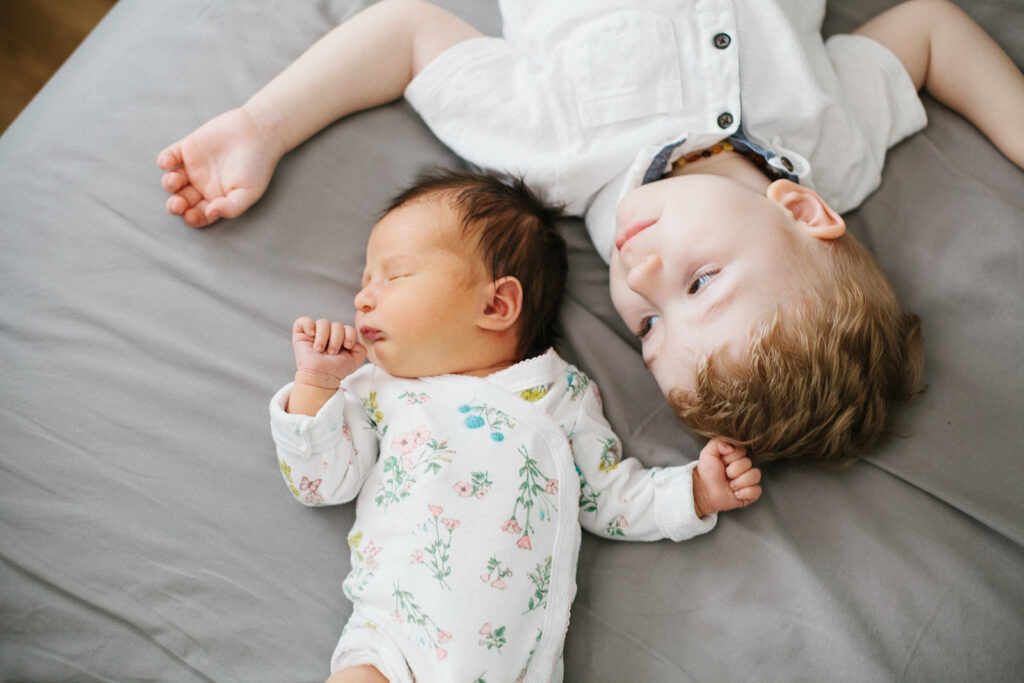 Baby girl sister laying down with baby brother on family bed during Lifestyle Newborn Session with Emily Louise Photography in Fort Wayne Indiana